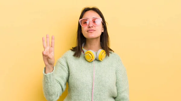 Jonge Spaanse Vrouw Glimlachend Vriendelijk Toont Nummer Drie Koptelefoon Zonnebril — Stockfoto