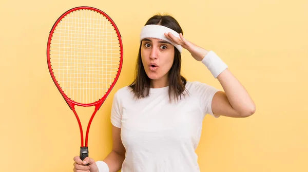 young hispanic woman looking happy, astonished and surprised. tennis concept