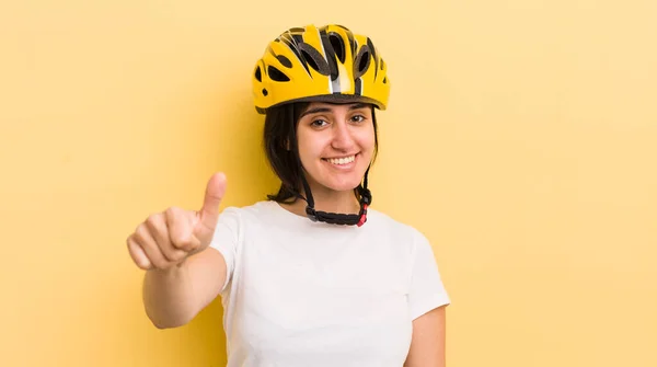 young hispanic woman feeling proud,smiling positively with thumbs up. bike helmet concept