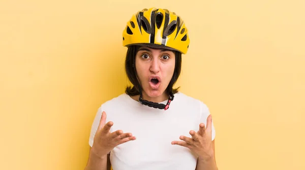 young hispanic woman amazed, shocked and astonished with an unbelievable surprise. bike helmet concept