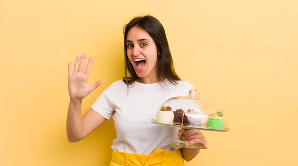 若いヒスパニック系の女性は笑顔で友好的に見えます5番目を示しています 家で作るケーキのコンセプト — ストック写真