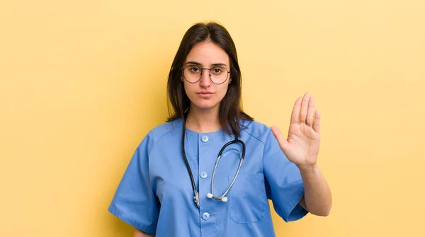 年轻的惊慌失措的女人看起来很严肃地展示着张开手掌的姿势 护士概念 — 图库照片