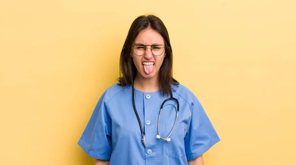 陽気で反抗的な態度を持つ若いヒスパニック系の女性冗談と舌を突き出す 看護師の概念 — ストック写真