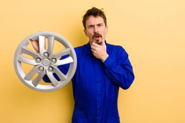 Ağzı ve gözleri açık ve eli çenesinde olan bir adam. araba tamircisi konsepti