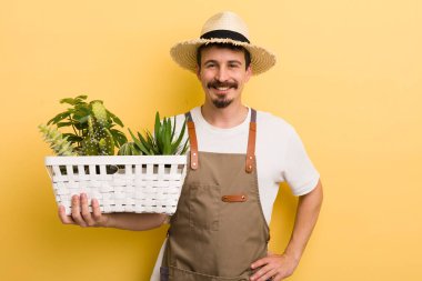 Adam mutlu bir şekilde gülümsüyor, eli kalçasında ve kendinden emin. Bahçıvan konsepti