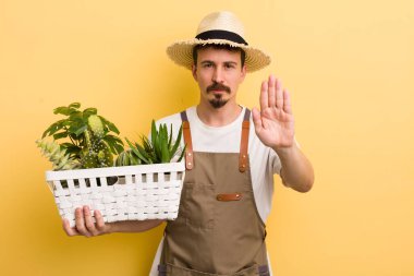 Adam ciddi görünüyor. Avuç içi gösteriyor. Durma hareketi yapıyor. Bahçıvan konsepti