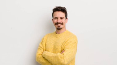 İspanyol asıllı genç adam kameraya çapraz kollarla gülümsüyor ve mutlu, kendinden emin, tatmin olmuş bir yüz ifadesi var.