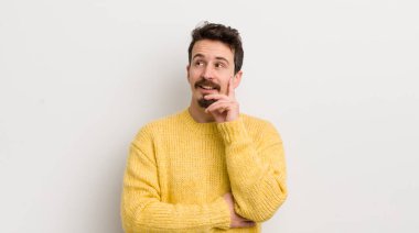 İspanyol genç adam mutlu bir şekilde gülümsüyor ve hayal kuruyor ya da şüphe ediyor.