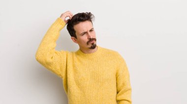 İspanyol genç adam şaşkın ve şaşkın hissediyor, başını kaşıyor ve yana bakıyor.