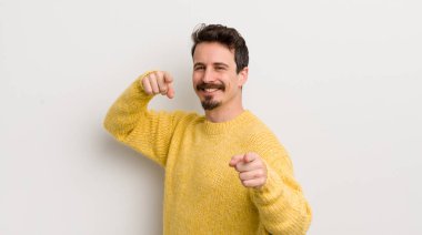 İspanyol genç adam mutlu ve kendinden emin, kamerayı iki eliyle gösteriyor ve gülüyor, seni seçiyor.