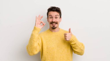 İspanyol genç adam kendini mutlu, şaşkın, tatmin olmuş ve şaşırmış hissediyor, iyi olduğunu gösteriyor ve jestler yapıyor, gülümsüyor