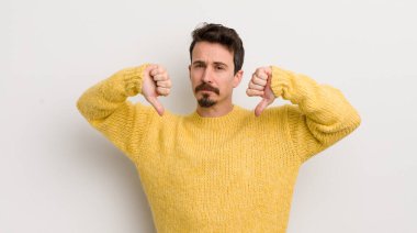 Hispanik genç adam üzgün, hayal kırıklığına uğramış ya da kızgın görünüyor, anlaşmazlık içinde başparmaklarını gösteriyor, hayal kırıklığına uğramış hissediyor