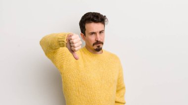 Hispanik genç adam sinirli, sinirli, hayal kırıklığına uğramış ya da hoşnutsuz, ciddi bir bakışla başparmağını kaldırıyor.