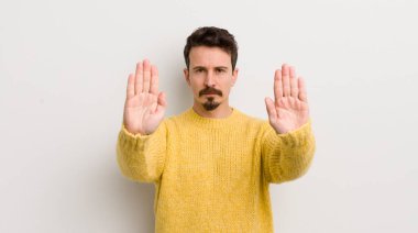 İspanyol genç adam ciddi, mutsuz, kızgın ve hoşnutsuz görünüyor. Girmeyi yasaklıyor ya da her iki avuçta da dur diyor.