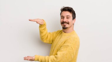 İspanyol genç adam gülümsüyor, mutlu, pozitif ve memnun, fotokopi alanında nesne ya da konsept tutuyor ya da gösteriyor