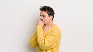 Boğazı ağrıyan ve grip belirtileri gösteren ağzı kapalı öksüren İspanyol genç bir adam.