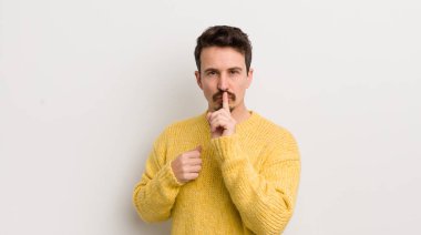 İspanyol genç adam ciddi görünüyor ve parmaklarını dudaklarına bastırıp sessizlik ya da sessizlik talep ediyor, sır saklıyor.