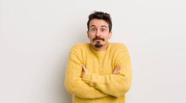 İspanyol genç adam omuz silkiyor, kafası karışık ve emin değil, kolları bağlı ve şaşkın görünüyor.