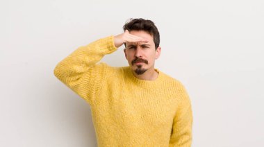 İspanyol genç adam şaşkın ve şaşkın bakıyor, el üstünde uzak bakıyor, izliyor ya da arıyor