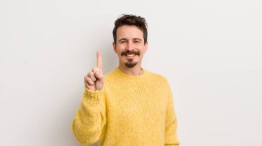 İspanyol genç adam gülümsüyor ve arkadaş canlısı görünüyor, bir numarayı gösteriyor veya ilk eli önde, geriye doğru sayıyor.