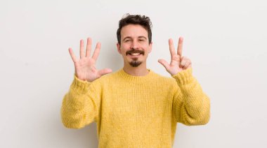 İspanyol genç adam gülümsüyor ve arkadaş canlısı görünüyor, 8 ya da 8 numarayı gösteriyor, eli önde, geri sayıyor.