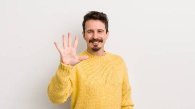 İspanyol genç adam gülümsüyor ve arkadaş canlısı görünüyor, 5 ya da 5 numarayı gösteriyor, eli önde, geriye doğru sayıyor.