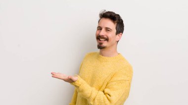 İspanyol genç adam neşeyle gülümsüyor, kendini mutlu hissediyor ve fotokopi uzayı içinde avucuyla bir konsept gösteriyor.