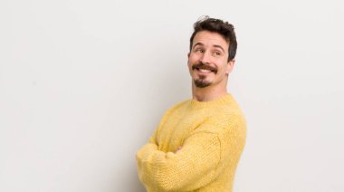 İspanyol genç adam neşeyle gülümsüyor, mutlu, tatmin olmuş ve rahatlamış hissediyor, kollarını kavuşturup yan tarafa bakıyor.