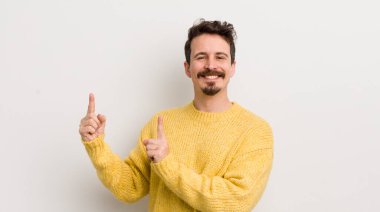 İspanyol genç adam mutlu bir şekilde gülümsüyor ve her iki elini de fotokopi alanında objeler gösteriyor.