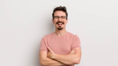 İspanyol genç adam mutlu, gururlu ve tatmin olmuş görünüyor. Kollarını kavuşturup gülümsüyor.