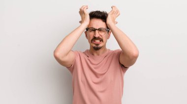 İspanyol genç adam stresli ve endişeli, depresif ve hayal kırıklığına uğramış hissediyor, iki elini de başa kaldırıyor.