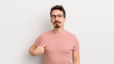 İspanyol genç adam gururlu, kendinden emin ve mutlu görünüyor, gülümsüyor ve kendini işaret ediyor ya da bir numaralı işareti yapıyor.