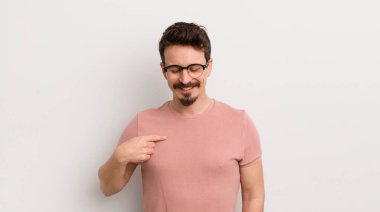 İspanyol genç adam neşeyle gülümsüyor, yere bakıyor ve göğsüne işaret ediyor.