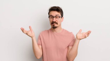 hispanic young man shrugging with a dumb, crazy, confused, puzzled expression, feeling annoyed and clueless