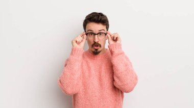 İspanyol genç adam şaşkın, şaşkın ve şaşırmış hissediyor, elinde şaşkın, inançsız bir bakışla gözlük tutuyor.