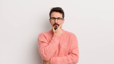 İspanyol genç adam ciddi, düşünceli ve güvensiz görünüyor, bir kolu çapraz ve çene üzerinde, seçenekleri tartıyor