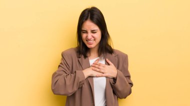 Genç İspanyol kadın üzgün, yaralı ve kalbi kırık görünüyor, iki elini de kalbe yakın tutuyor, ağlıyor ve bunalımda.