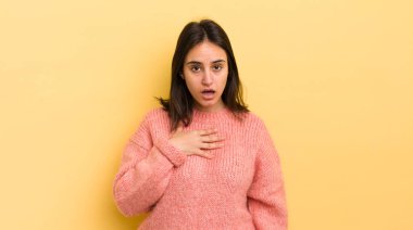 Genç İspanyol kadın şaşkın, şaşkın ve şaşırmış hissediyor, elleri göğsünde ve ağzı açık, kim olduğunu söylüyor, ben?