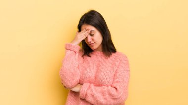Genç İspanyol kadın stresli, utanmış ya da üzgün görünüyor, baş ağrısı var, yüzünü eliyle kapatıyor.