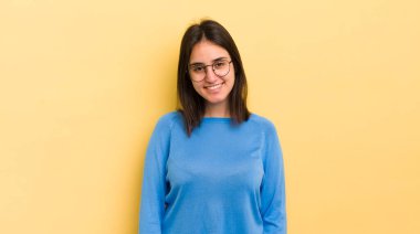 Genç İspanyol kadın neşeli, mutlu, kendinden emin ve rahat bir ifadeyle gülümsüyor.