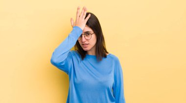 young hispanic woman raising palm to forehead thinking oops, after making a stupid mistake or remembering, feeling dumb