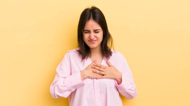 Genç İspanyol kadın üzgün, yaralı ve kalbi kırık görünüyor, iki elini de kalbe yakın tutuyor, ağlıyor ve bunalımda.