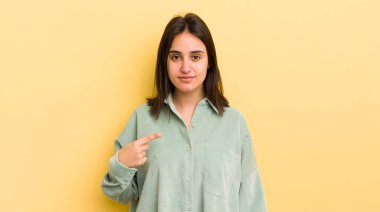 Genç İspanyol kadın gururlu, kendinden emin ve mutlu görünüyor, gülümsüyor ve kendini işaret ediyor veya bir numaralı işareti yapıyor.