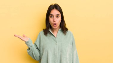 Genç İspanyol kadın şaşırmış ve şoka uğramış görünüyor, çenesi düşmüş, eli açık bir objeyi tutuyor.