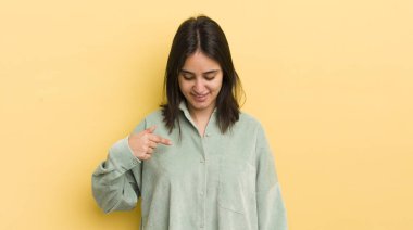 Genç İspanyol kadın neşeyle gülümsüyor, yere bakıyor ve göğsüne işaret ediyor.