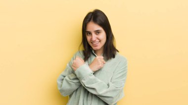 Genç İspanyol kadın sevinçle gülümsüyor ve kutluyor, yumruklarını sıkmış ve kollarını kavuşturmuş, mutlu ve pozitif hissediyor.