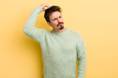 Genç İspanyol adam şaşkın ve şaşkın hissediyor, başını kaşıyor ve yana bakıyor.