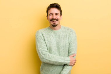 Genç İspanyol adam utangaç ve neşeli bir şekilde gülüyor, arkadaş canlısı ve olumlu ama güvensiz bir tavırla.