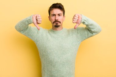 Genç İspanyol adam üzgün, hayal kırıklığına uğramış ya da kızgın görünüyor. Anlaşmazlık içinde başparmaklarını gösteriyor. Hayal kırıklığına uğramış hissediyor.