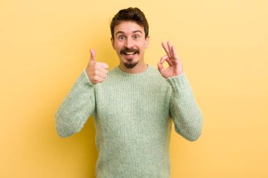 Genç İspanyol adam kendini mutlu, şaşkın, tatmin olmuş ve şaşırmış hissediyor, tamam gösteriyor ve el kol hareketleri yapıyor, gülümsüyor